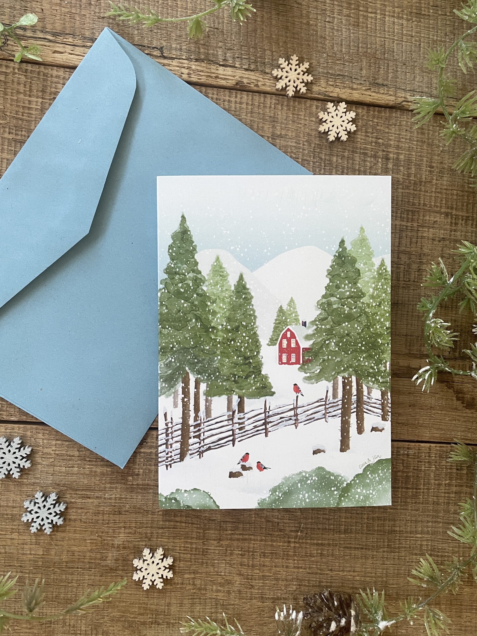 Handillustrierte Klappkarte Winterglück rotes Holzhaus verschneite Berglandschaft Gimpel Tannen von Ann und Jan Kuvert Blau