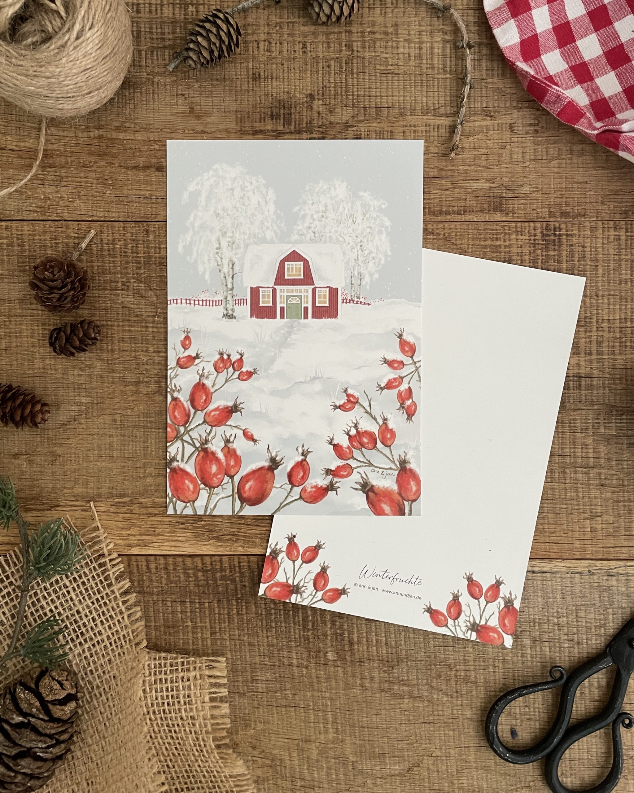 Postkarte Winterfrüchte handillustriert. Rotes Schwedenhaus und Hagebutten in verschneiter Winterlandschaft. Rückseite beschreibbar